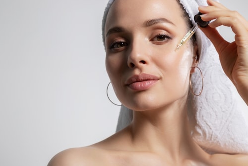 woman in bath towel on head applying oil serum